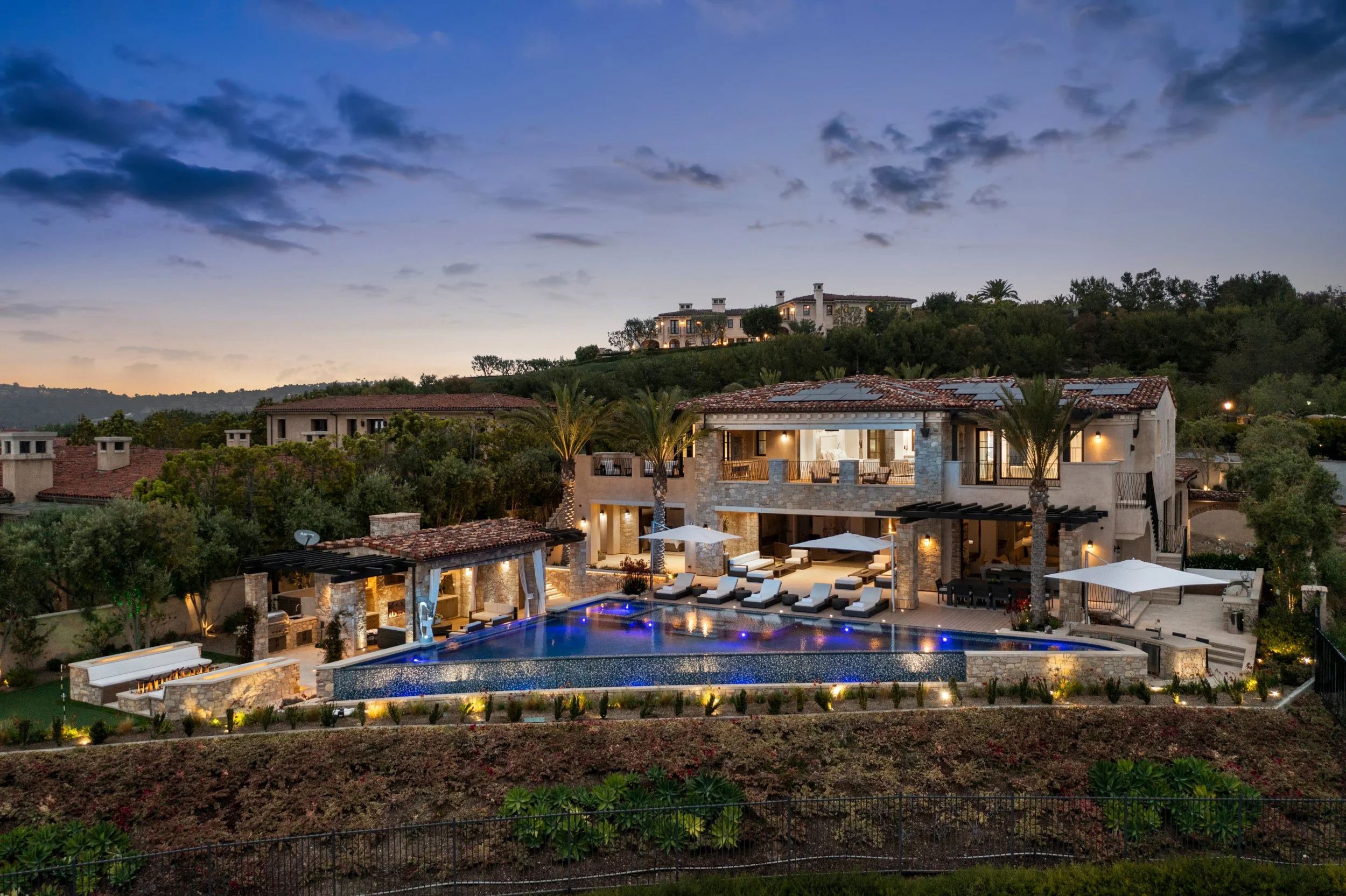 Mediterranean hillside home at dusk with a lit triangular infinity pool and outdoor lounge chairs.