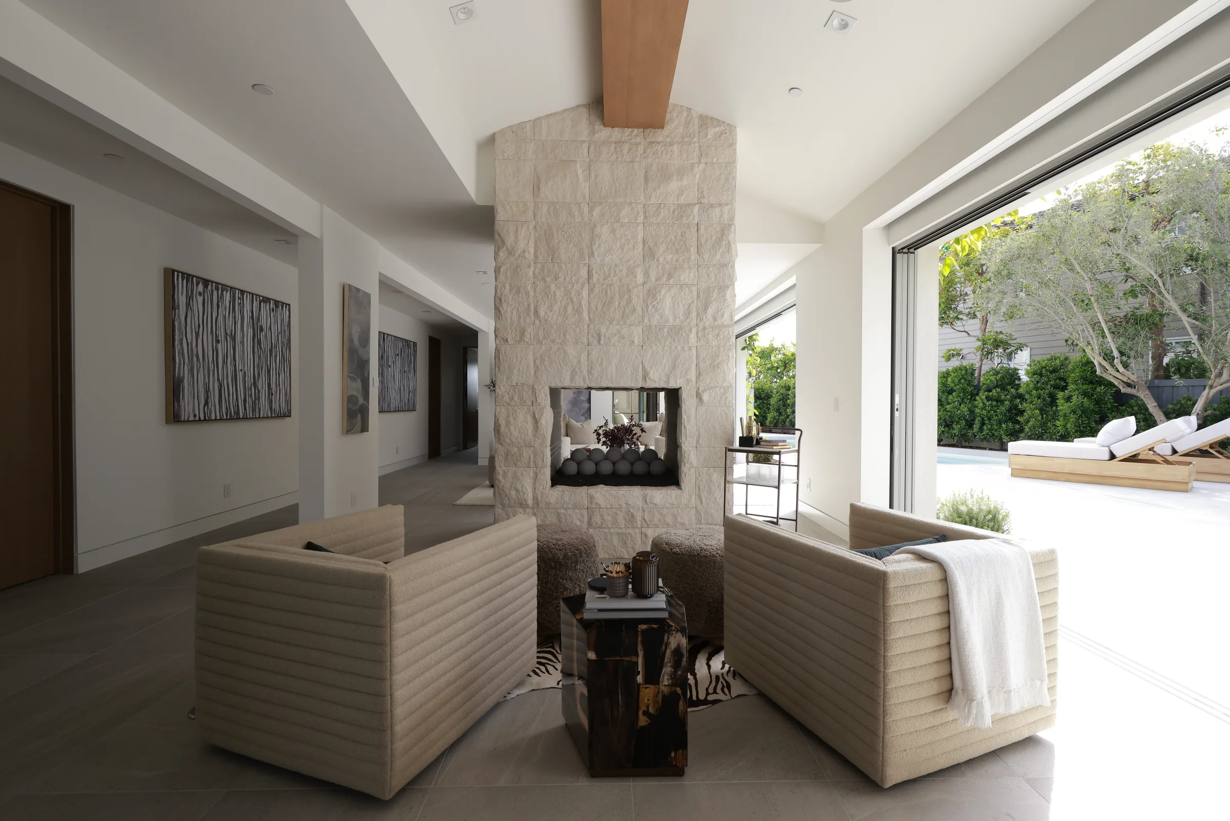 Stone fireplace lounge with textured chairs and a fully open glass wall to a sunlit garden patio.